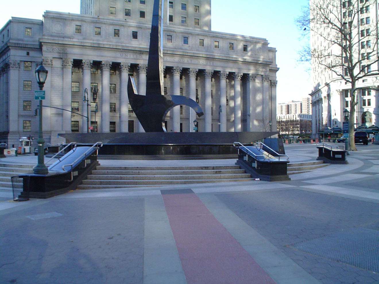 Fountain: circular basin supports a colossal composition consisting of a horizontal member lying across the basin with one end resting against a boulder; the horizontal form supports a tall, vertical form resembling an inverted dagger; plaque