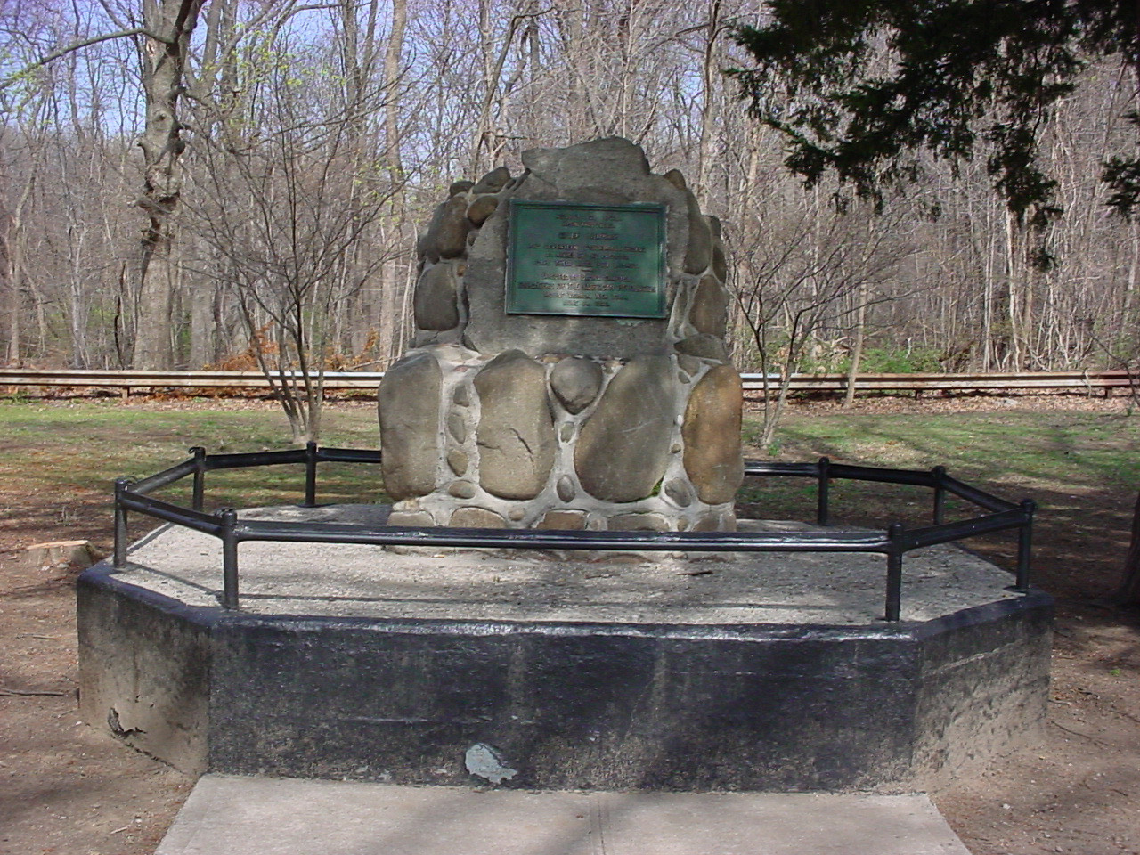 Boulder-like form (cairn) bearing a plaque, on a low base