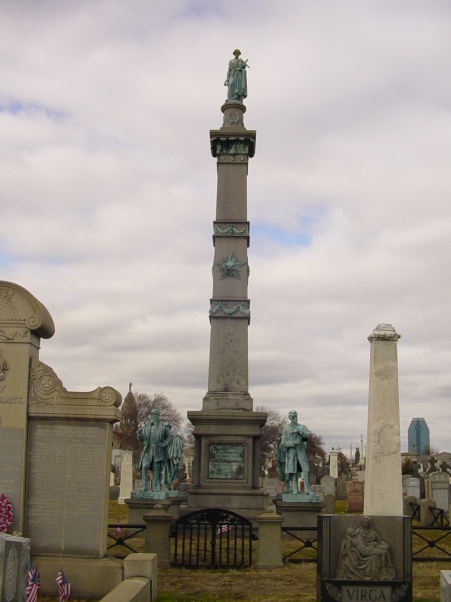 Obelisk with applied decorations surmounted by figure (heroic scale), die with decorations on all four faces (?), graduated base; four figures (life size) on corner pedestals; fenced square with four cannons at corners and four eagles on corner piers