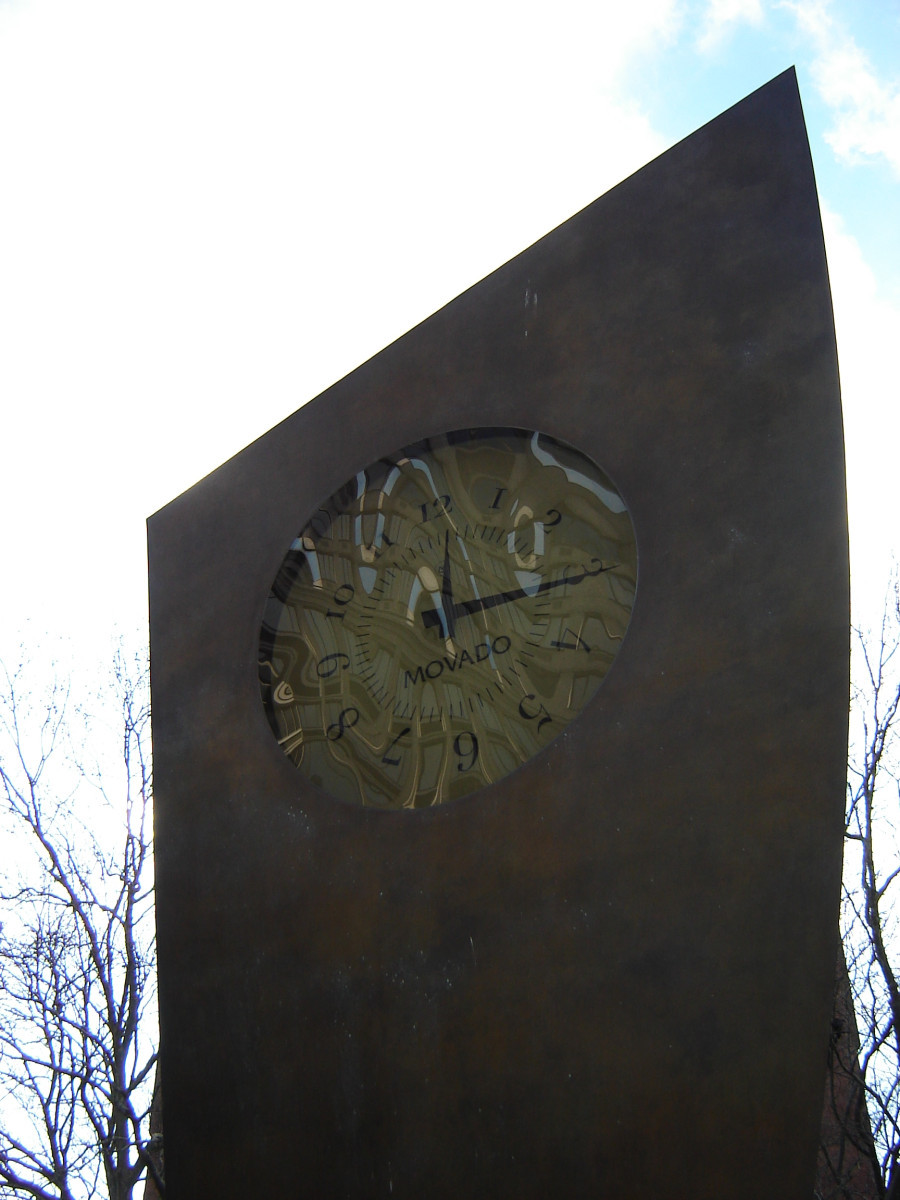 Four clocks set in three vertical faces of oblique trianguloid form on oblique trianguloid base