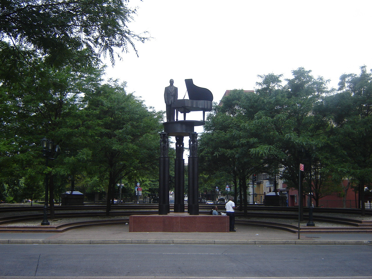 Standing figure (heroic scale) before a grand piano on a circular platform supported by three groups of three caryatids on three triform columns, integral plinth, two plaques on pedestal