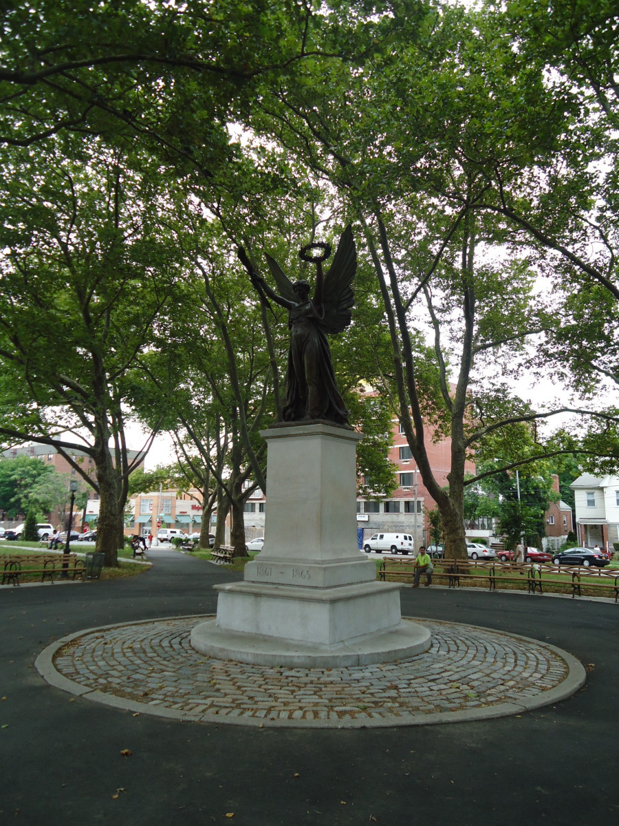 Standing angel figure (over life-size) holding a laurel wreath in her left hand and a palm bough in her right,, on integral plinth on pedestal