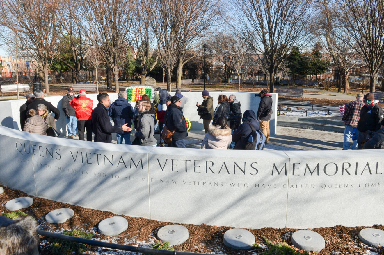 Two semi-circular granite walls inscribed with honor roll of 371 names of those who died, historical timeline, bamboo motif, memorial name, and military crests, surrounding a sunken seating area and plaza inscribed with a map.