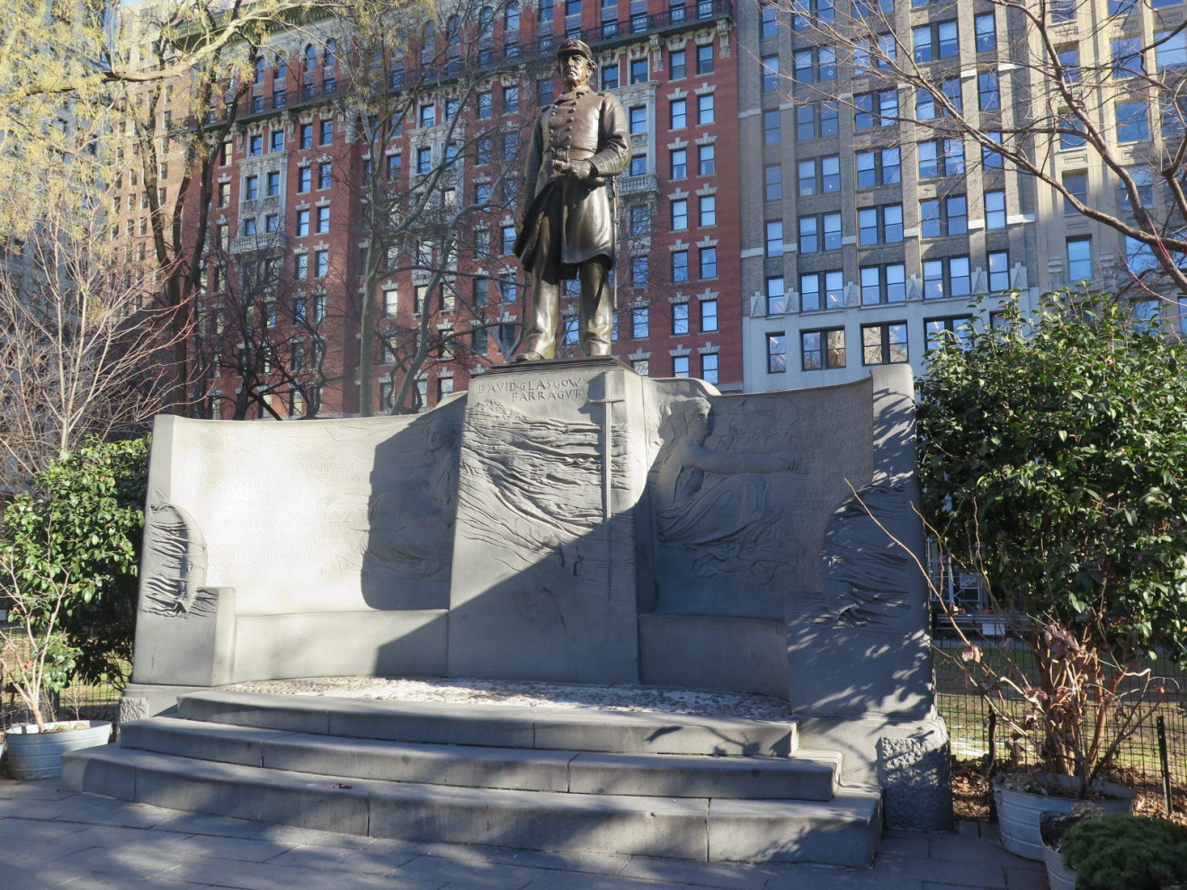 Standing figure (over life-size) with integral plinth, on pedestal with extended exedra wings; pedestal has bas-relief of sword in ocean waves; each wing  has a life-size bas-relief of seated female figure