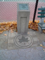 Bronze plaque on pillar with incised, green-painted leaf at bottom in pavement