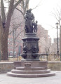 Group of three figures---standing mother holds baby on right arm with infant at her left side---(over life-size) on an ornamented, octagonal pedestal with a lion head fountain and a basin on each of  four sides; formerly a working drinking fountain