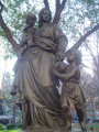 Group of three figures---standing mother holds baby on right arm with infant at her left side---(over life-size) on an ornamented, octagonal pedestal with a lion head fountain and a basin on each of  four sides; formerly a working drinking fountain