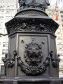 Group of three figures---standing mother holds baby on right arm with infant at her left side---(over life-size) on an ornamented, octagonal pedestal with a lion head fountain and a basin on each of  four sides; formerly a working drinking fountain