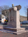 Standing, winged female figure (heroic scale) on pedestal, in front of stele, benches at sides