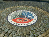 2-part granite column with star in the middle; paved plaza has semi-circular granite wall and inset mosaic design