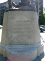 Standing figure (over life-size) contemplates a grave marked by a cross, on integral plinth, on pedestal  with plaque