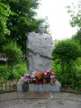 Bust emerging from a rough-hewn block, so it appears to be enshrouded up to the shoulders in a map of Poland, two plaques in pavement at front