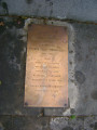 Bust emerging from a rough-hewn block, so it appears to be enshrouded up to the shoulders in a map of Poland, two plaques in pavement at front