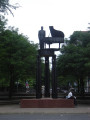 Standing figure (heroic scale) before a grand piano on a circular platform supported by three groups of three caryatids on three triform columns, integral plinth, two plaques on pedestal