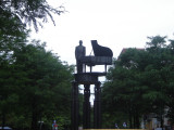 Standing figure (heroic scale) before a grand piano on a circular platform supported by three groups of three caryatids on three triform columns, integral plinth, two plaques on pedestal