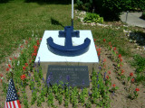 Two inscribed markers in ground in front of two cement plinths with blue anchors in relief