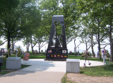 Obelisk with cutout in shape of soldier on base with mosaic flags, two plaques on two markers situated in circular plaza (axis aligned with Statue of Liberty)