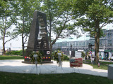 Obelisk with cutout in shape of soldier on base with mosaic flags, two plaques on two markers situated in circular plaza (axis aligned with Statue of Liberty)