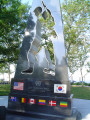 Obelisk with cutout in shape of soldier on base with mosaic flags, two plaques on two markers situated in circular plaza (axis aligned with Statue of Liberty)