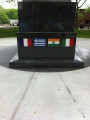 Obelisk with cutout in shape of soldier on base with mosaic flags, two plaques on two markers situated in circular plaza (axis aligned with Statue of Liberty)