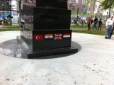 Obelisk with cutout in shape of soldier on base with mosaic flags, two plaques on two markers situated in circular plaza (axis aligned with Statue of Liberty)