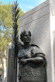 Standing figure with shield on integral plinth before stele; two tablets,