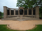 Group of two figures on pedestal before a high, arced wall; two benches; altar; six large plaques; one small plaque; paving