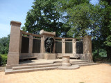 Group of two figures on pedestal before a high, arced wall; two benches; altar; six large plaques; one small plaque; paving