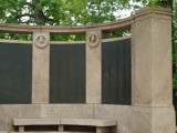 Group of two figures on pedestal before a high, arced wall; two benches; altar; six large plaques; one small plaque; paving