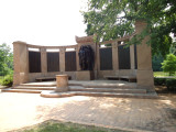 Group of two figures on pedestal before a high, arced wall; two benches; altar; six large plaques; one small plaque; paving