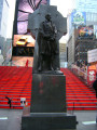 Standing figure (over life size) before a Celtic cross, on a pedestal, on a base, on a platform with seat at  rear, approached by three steps