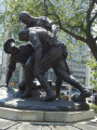 Group of three doughboy figures (over life-size) with integral plinth on a low base that rests on a circular pedestal; twenty plaques facing upward and carrying the names of the dead surround  the group