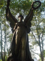 Standing angel figure (over life-size) holding a laurel wreath in her left hand and a palm bough in her right,, on integral plinth on pedestal