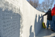 Two semi-circular granite walls inscribed with honor roll of 371 names of those who died, historical timeline, bamboo motif, memorial name, and military crests, surrounding a sunken seating area and plaza inscribed with a map.