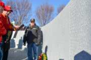 Two semi-circular granite walls inscribed with honor roll of 371 names of those who died, historical timeline, bamboo motif, memorial name, and military crests, surrounding a sunken seating area and plaza inscribed with a map.