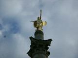 Corinthian column surmounted by standing figure (heroic scale), on pedestal with four-corner extensions bearing urns; fronted by right and left base elements each with a bas-relief; terrace with steps at front has six urns