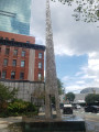 Tall obelisk with variegated surface on a pentagonal base; plaque