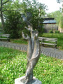 A hand pointing down supports a group of three hands pointing upward with the higher, middle hand supporting a dove with wings spread and starting to fly, on a pedestal