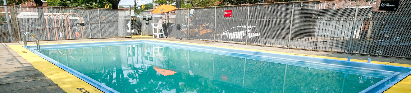 An empty children's pool is located in a park next to a quiet city street.