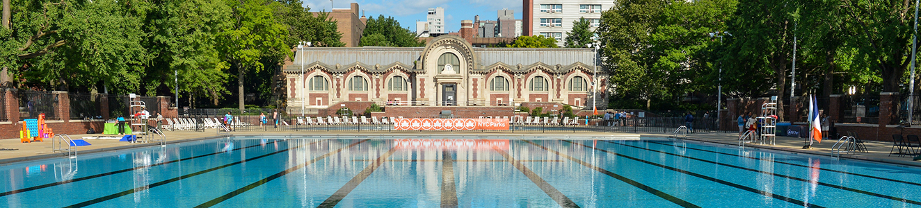 A clear blue outdoor pool with an old-fashioned bath house at the other end.