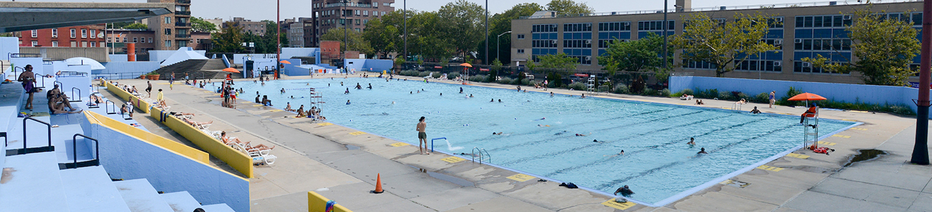 A large municipal pool with a blue overhang in the middle of a city block.