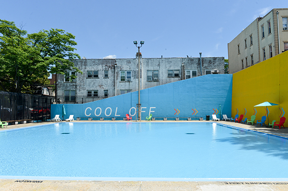 Fisher Pool’s back wall reads “cool off” with arrows leading to the other wall decals. Around the pool are brightly-colored lounge chairs.