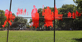 This artwork is an orange-colored mesh folded and sewn unto the baseball field's fence in the pattern of a snapshots of people in the park.