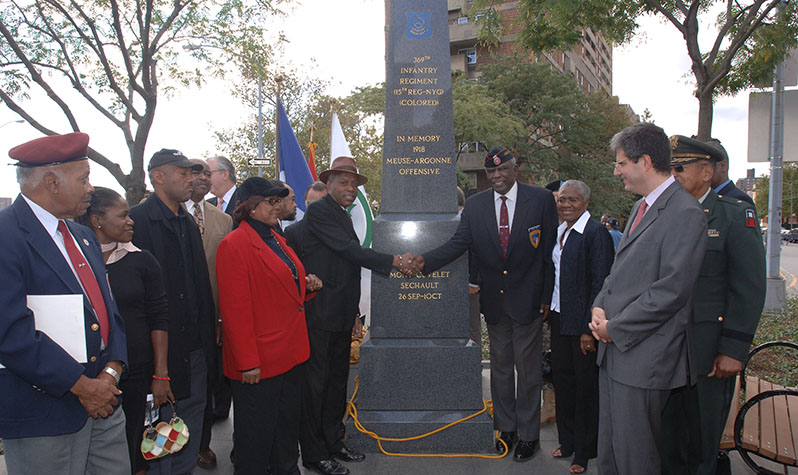 A group of African-American veterans, some in uniform, surround a 12-foot tall black granite obelisk with gilded inscriptions.