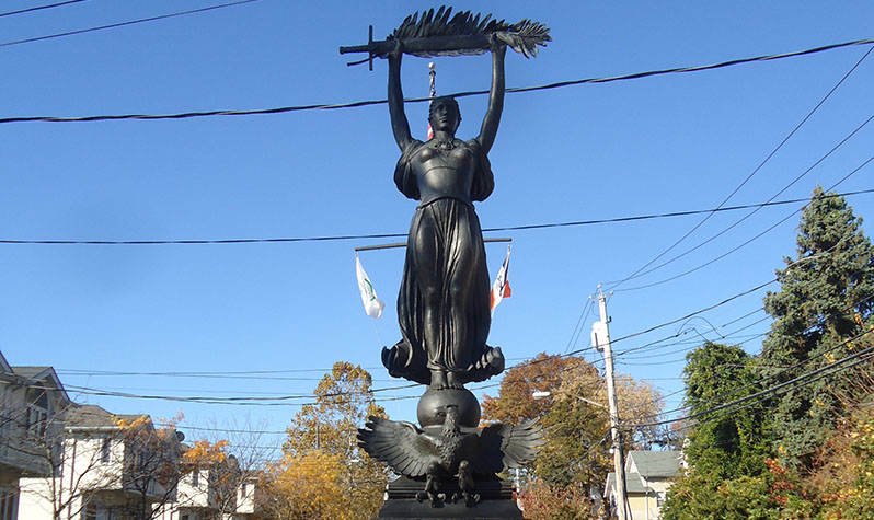 A female figure in bronze stands on a granite pedestal holding a sword and palm frond high in the air while an eagle with its wings spread sits at her feet.