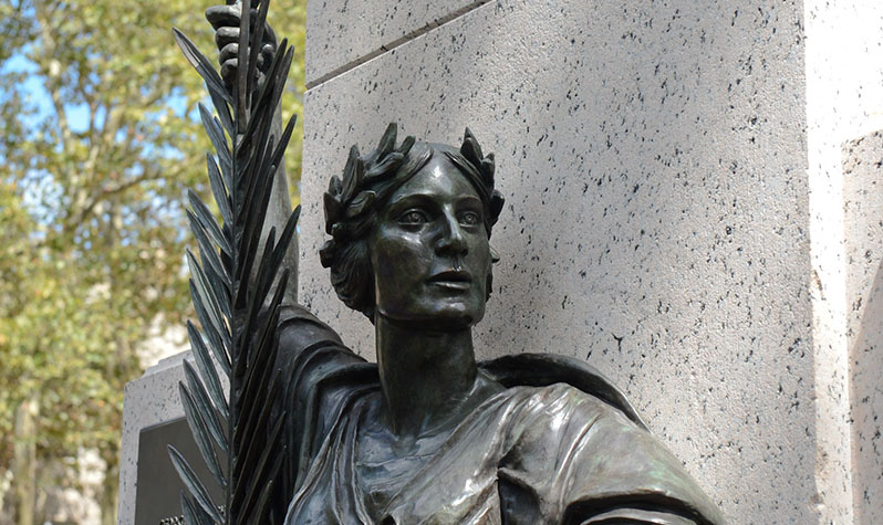 Cropped photo showing the head and bust of a bronze statue of a female figure wearing a laurel wreath crown and holding a palm frond.