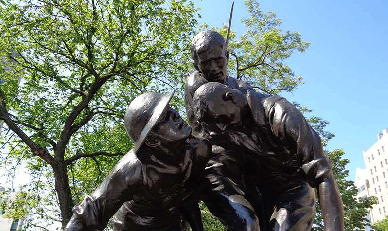 A bronze statue depicting two soldiers, one kneeling and one standing, who support a third slumping comrade in battle.