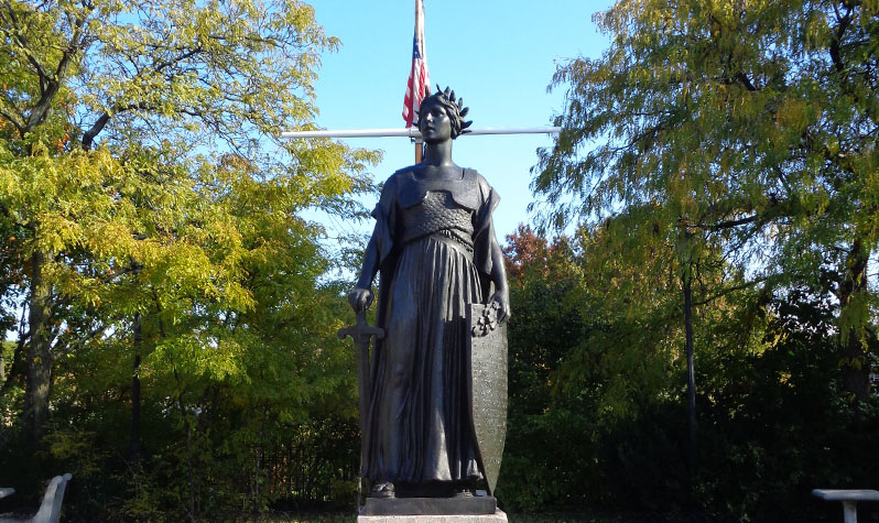 A seven-foot-tall female figure bears a sword in her right hand and an inscribed shield in her left.