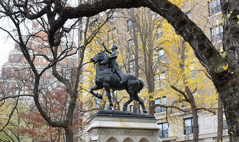 The statue, on a pedestal, depicts Joan of Arc riding a horse with a sword in hand and pointed in the air.