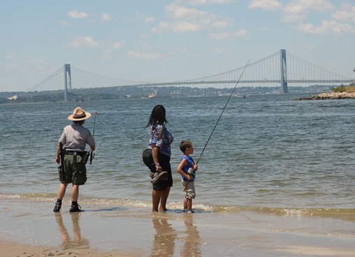 A park ranger shows a family how to use fishing rod to go fishing at the waterfront